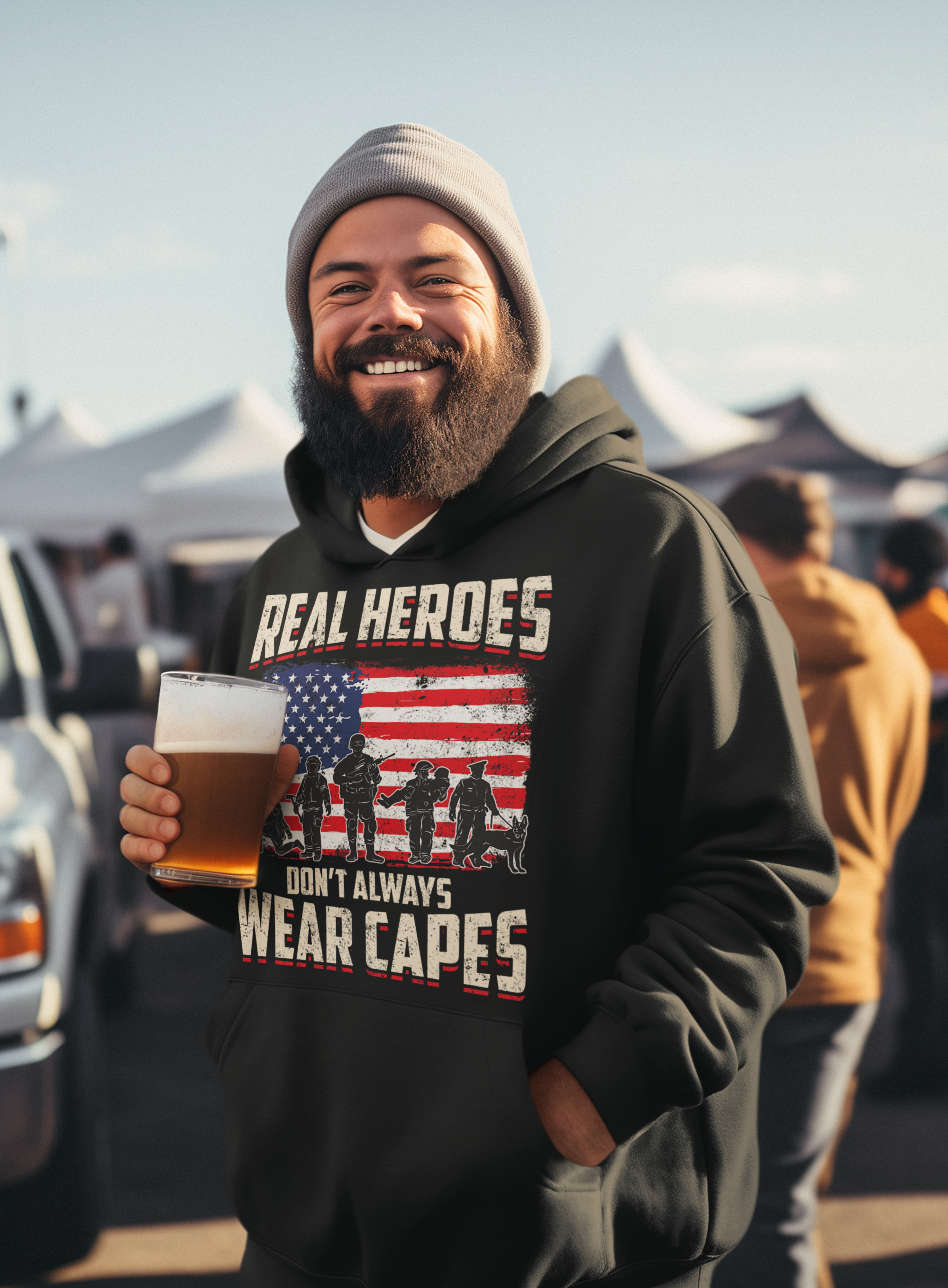 Man wearing a hoodie with a graphic and text, holding a beer at an outdoor event.