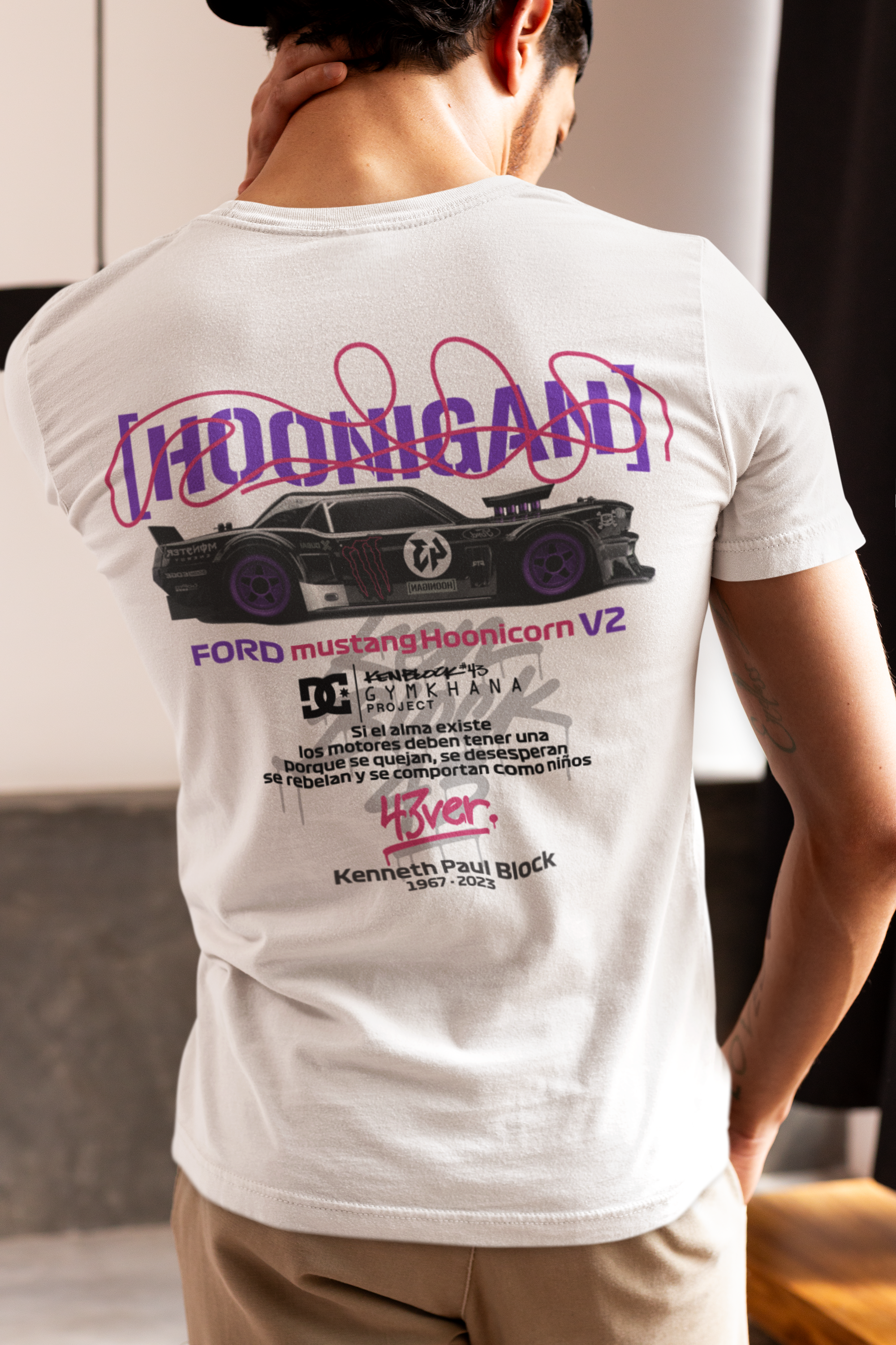 Person wearing a white t-shirt with a graphic design on the back, standing indoors.