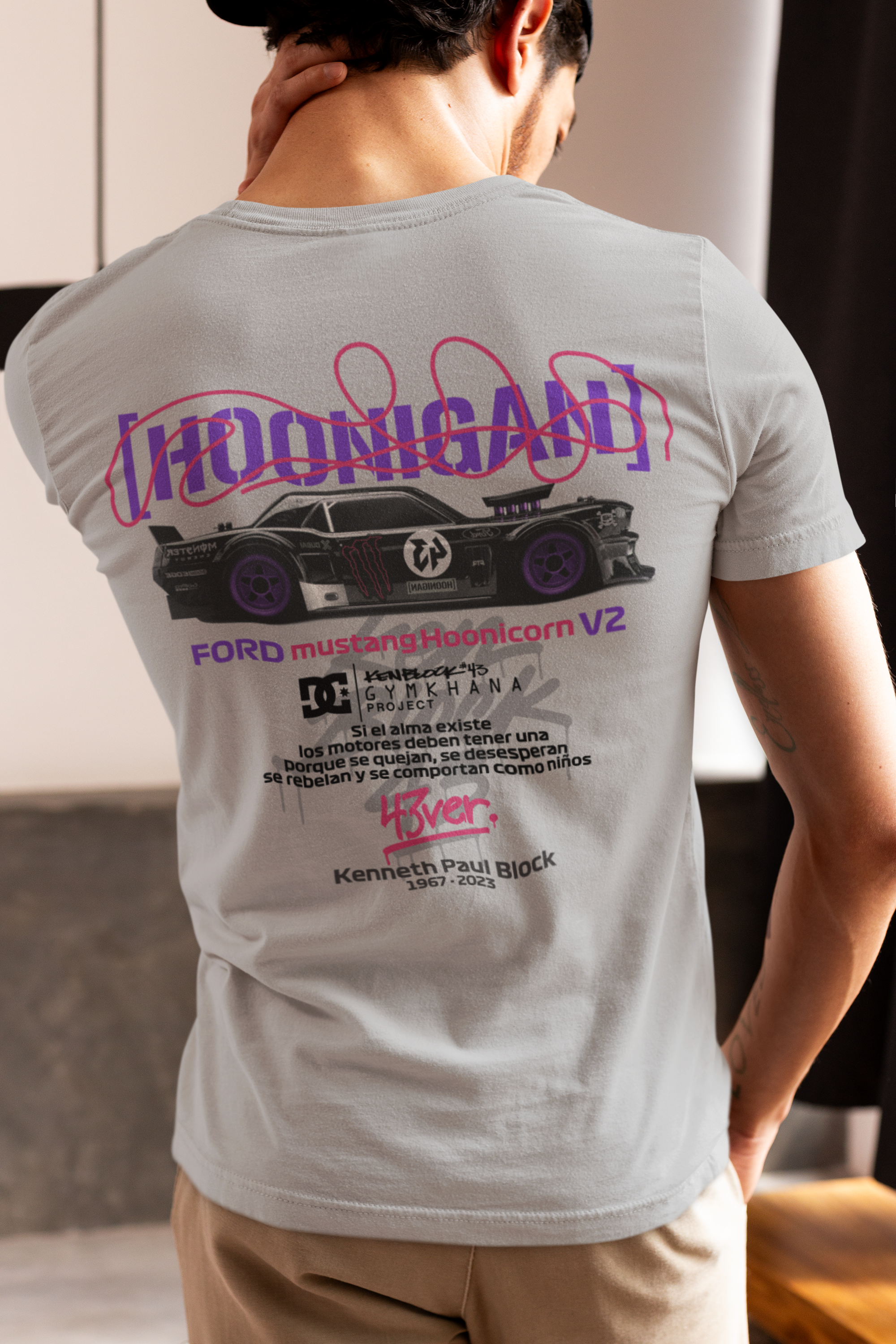 Person wearing a gray t-shirt with a graphic design on the back, standing indoors.