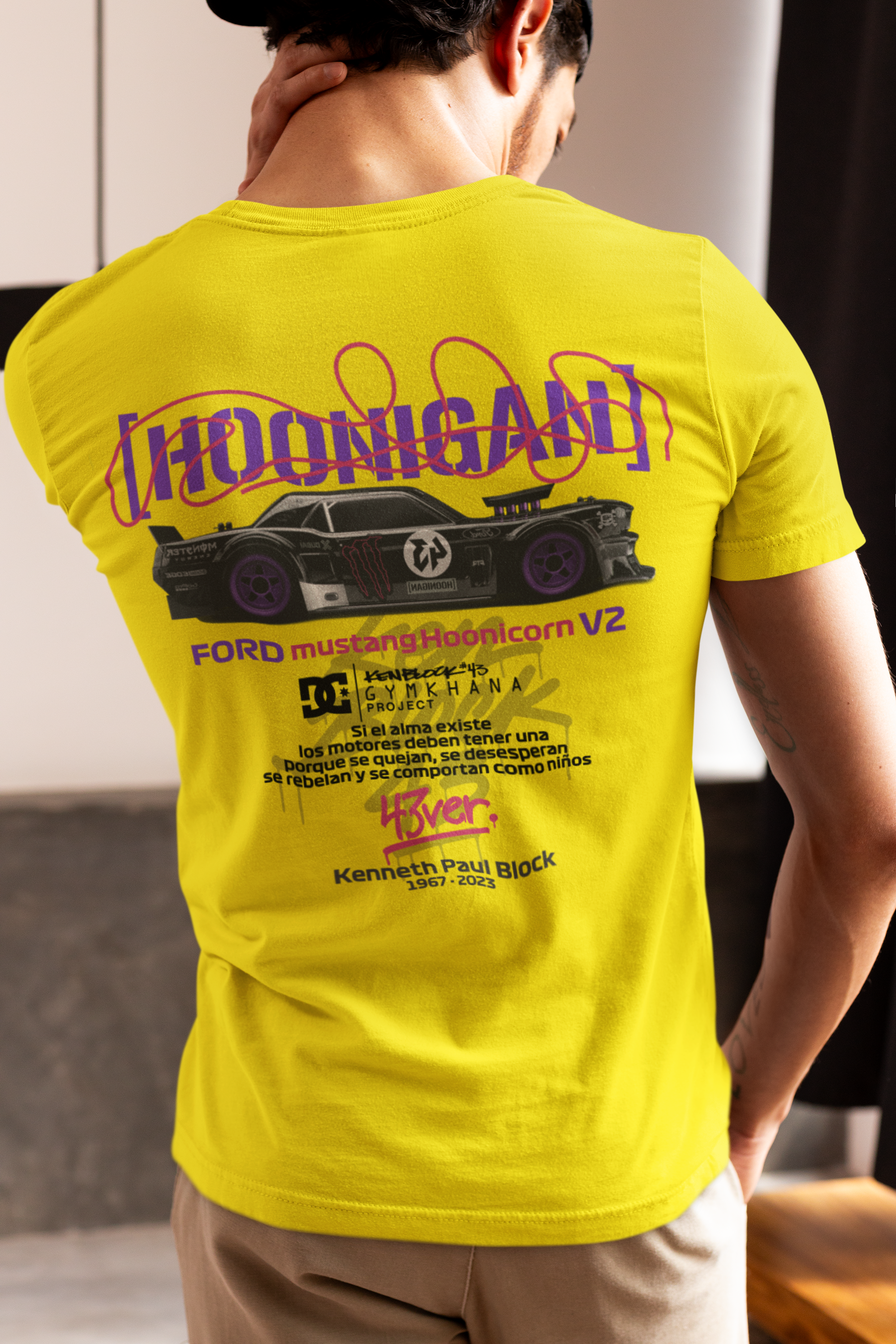 Person wearing a yellow t-shirt with a graphic design on the back, standing indoors.