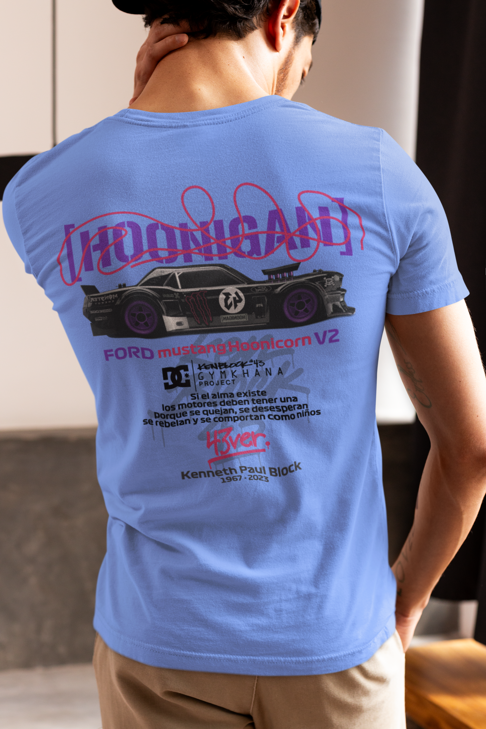 Person wearing a blue t-shirt with a graphic design on the back, standing indoors.