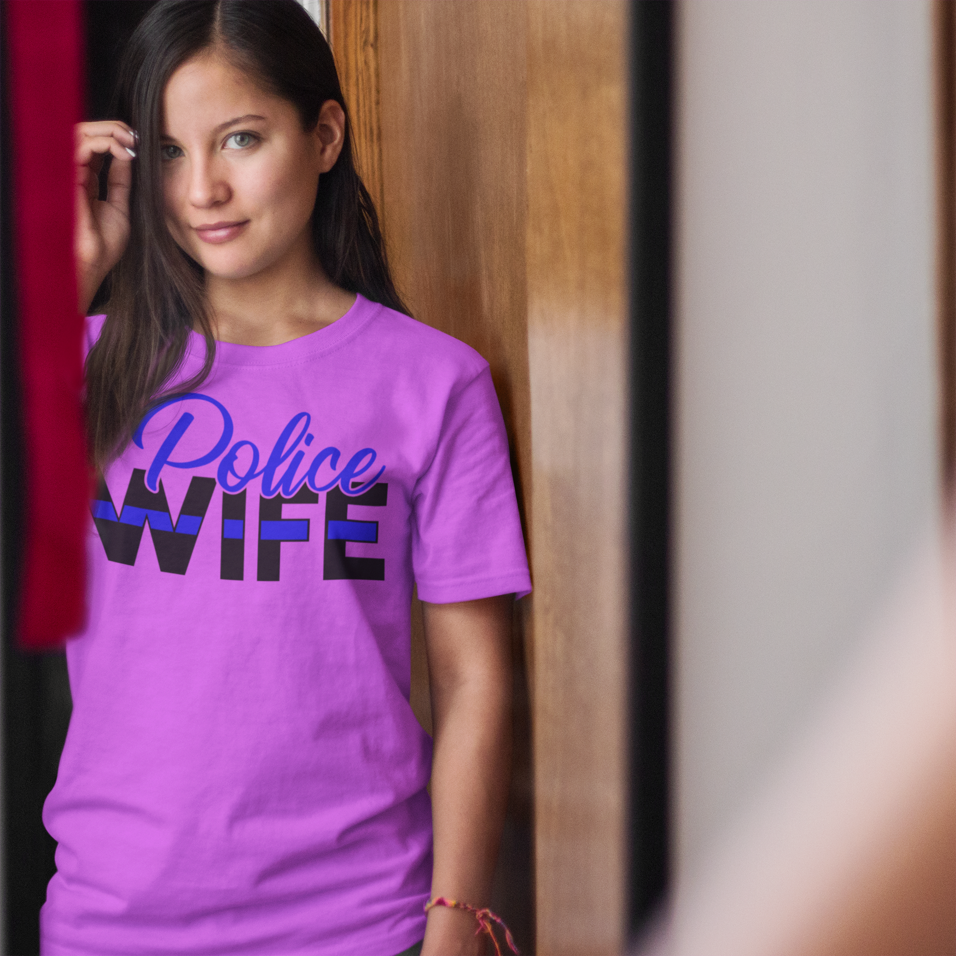 Woman wearing a purple 'Police Wife' t-shirt against a wooden panel background