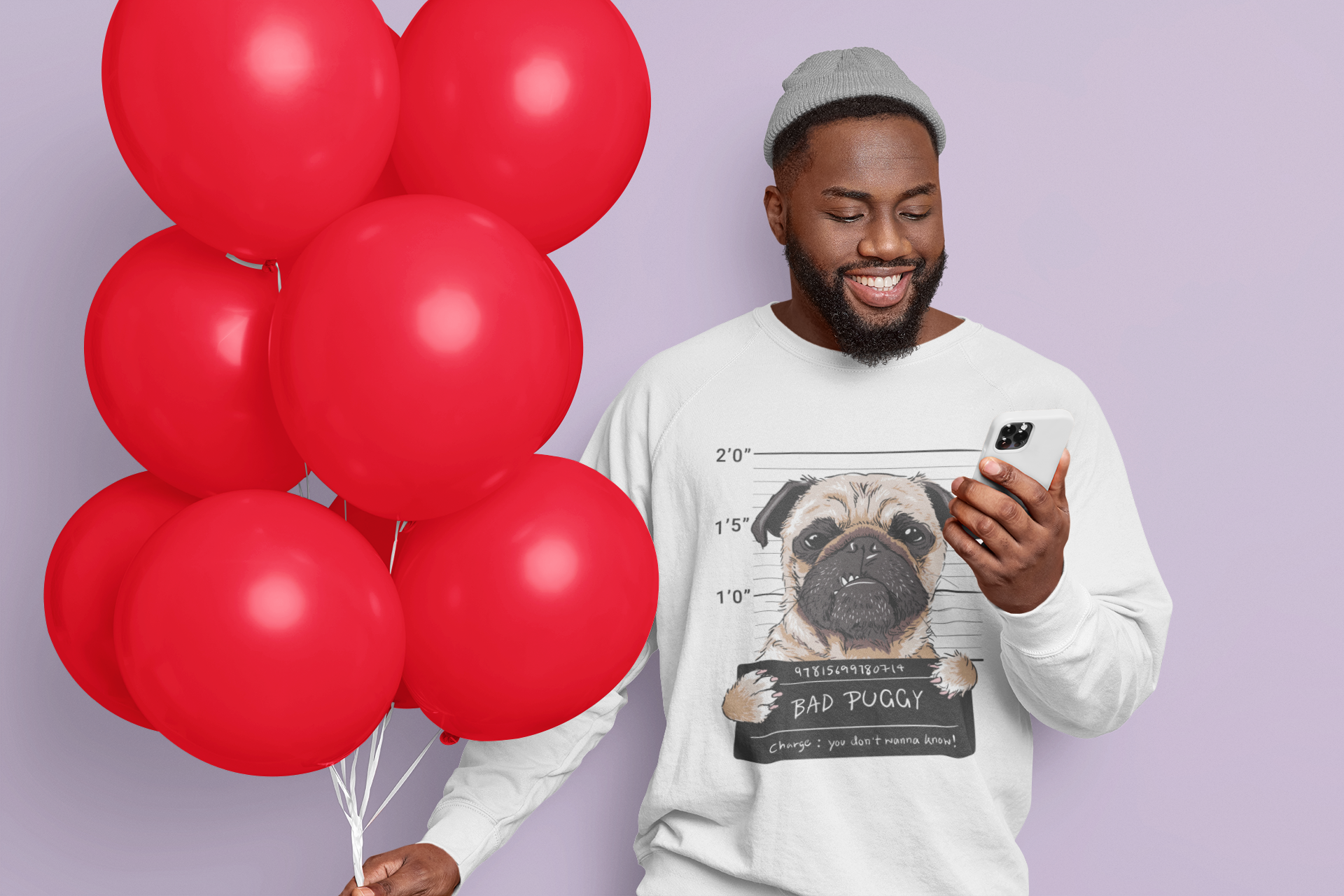 Man holding red balloons and a phone, wearing a sweatshirt with a pug graphic, on a light purple background