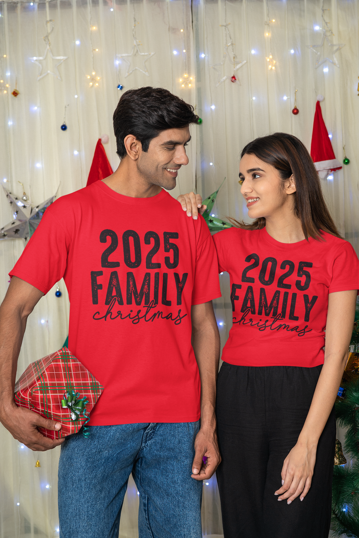 Two people wearing red '2025 Family Christmas' shirts in front of a festive background.