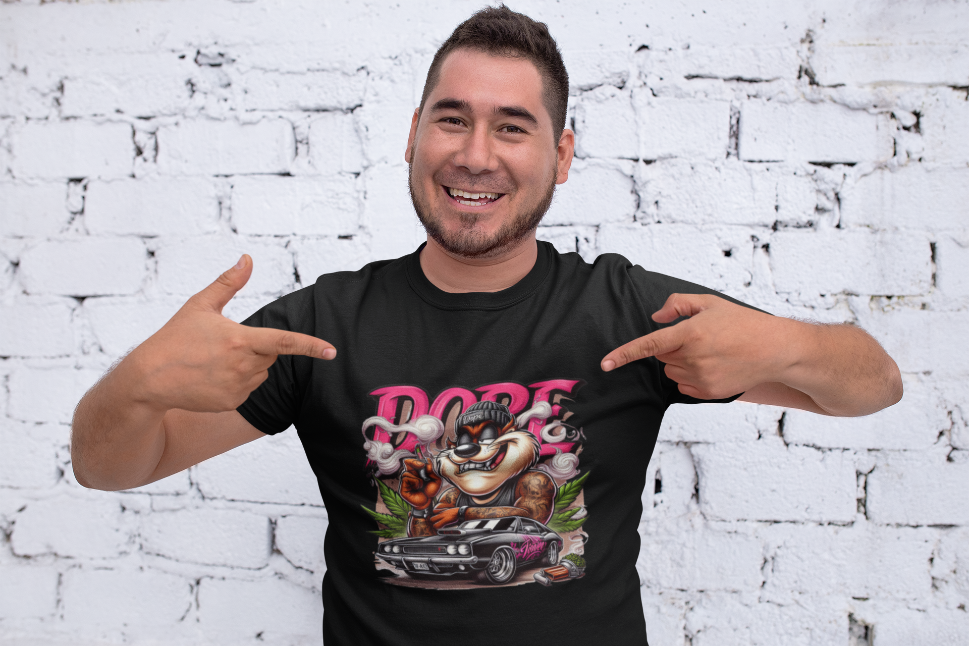 Man wearing a black t-shirt with colorful graphic design and 'DOPE' text, pointing at the shirt against a white brick wall.