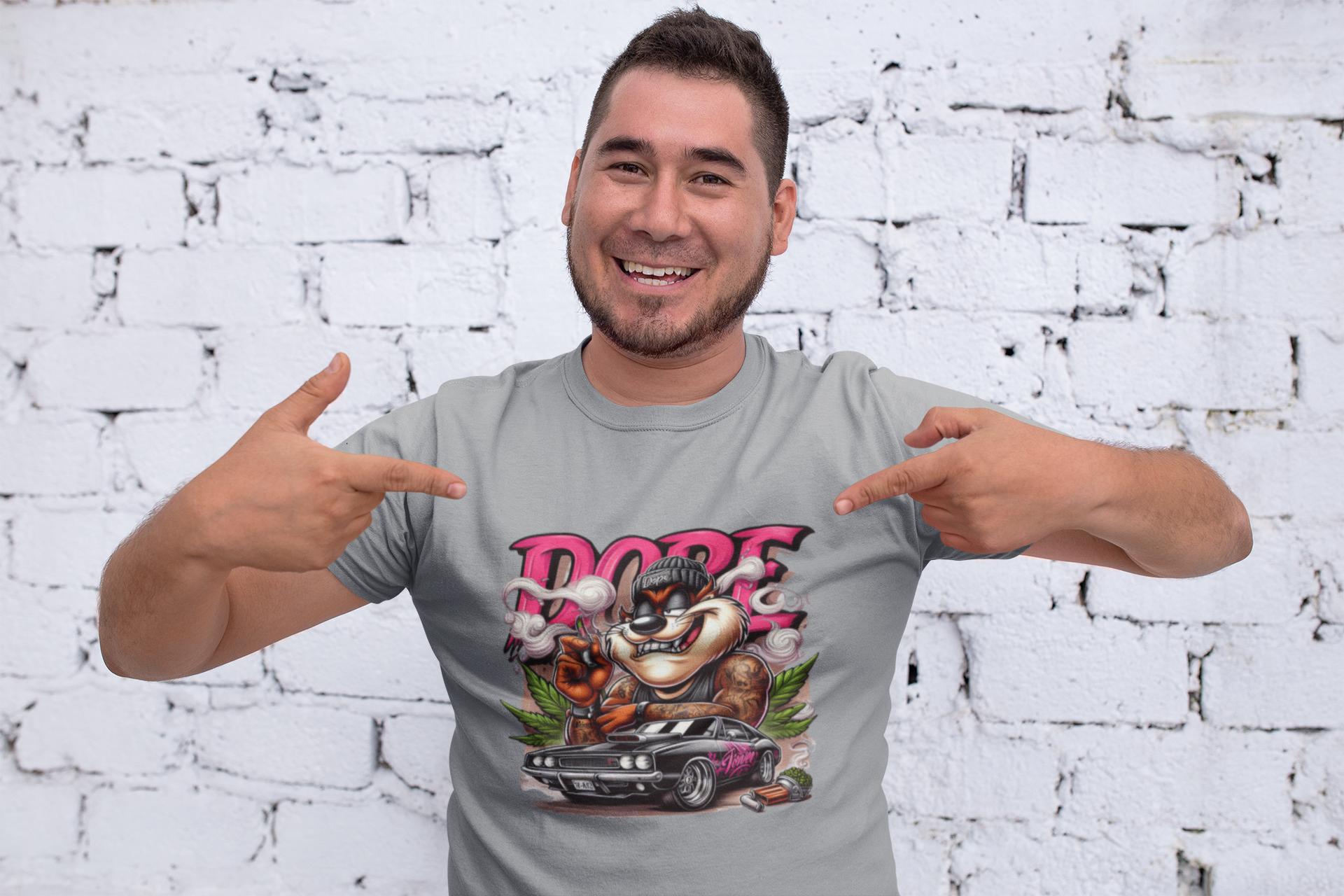 Man wearing a gray t-shirt with a graphic design pointing at himself against a white brick wall.