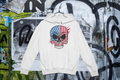 White hoodie with skull and American flag design on a graffiti-covered wall.
