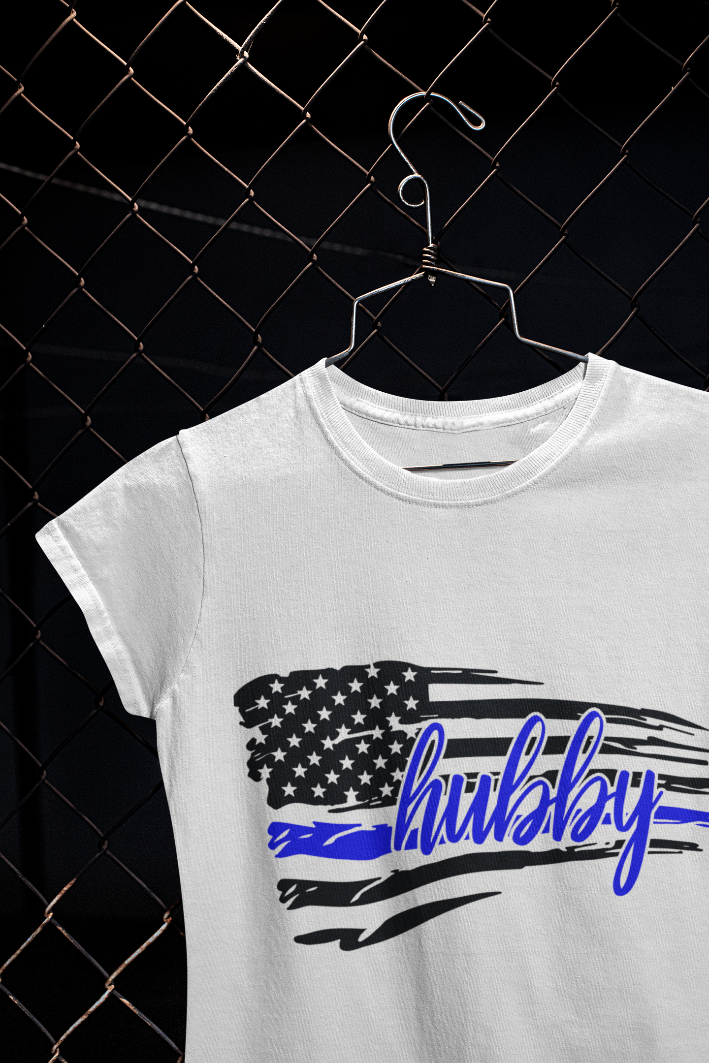 White t-shirt with American flag and 'hubby' text on a hanger against a black mesh background