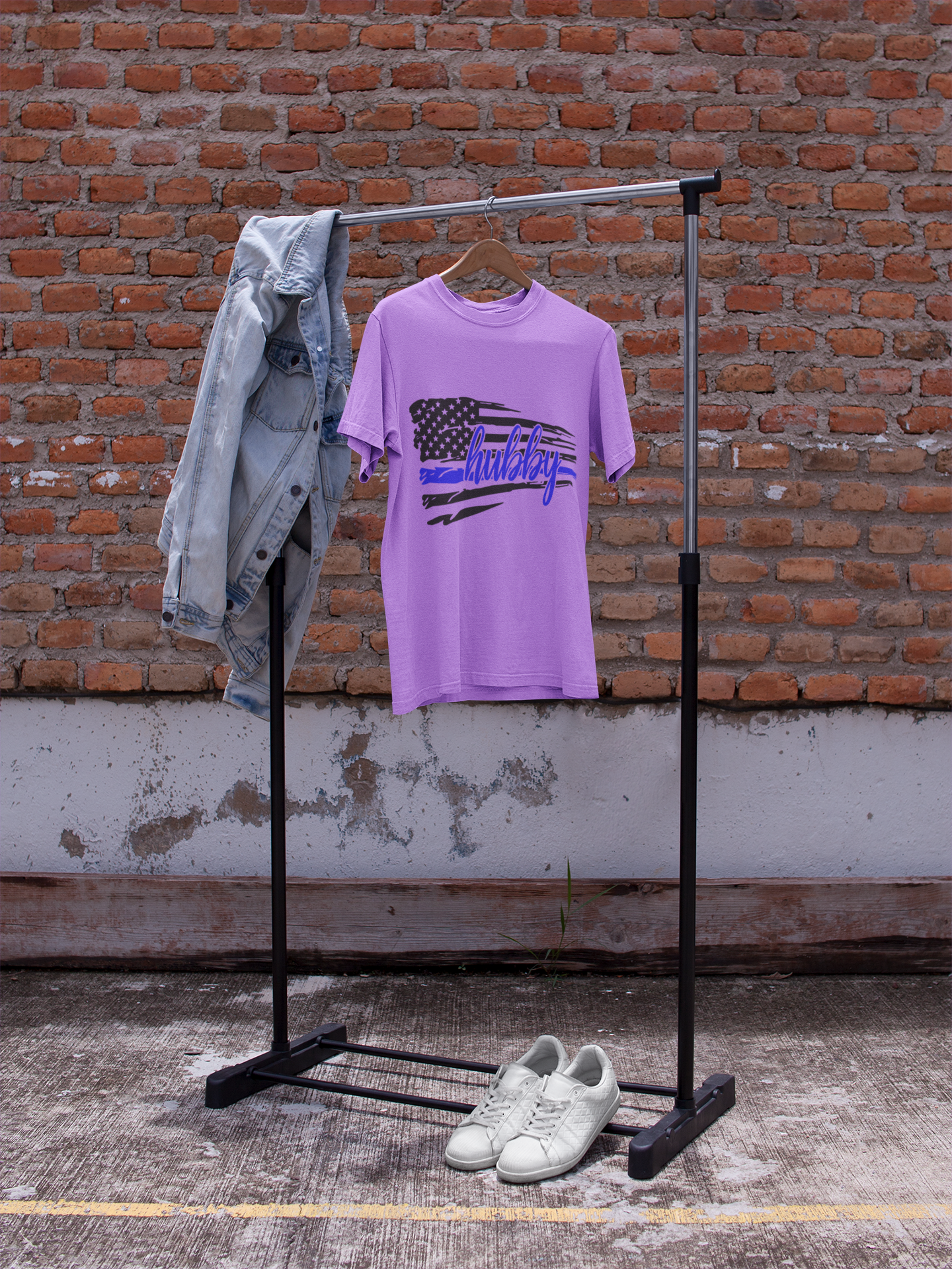 Purple t-shirt with graphic design on a black clothing rack against a brick wall.