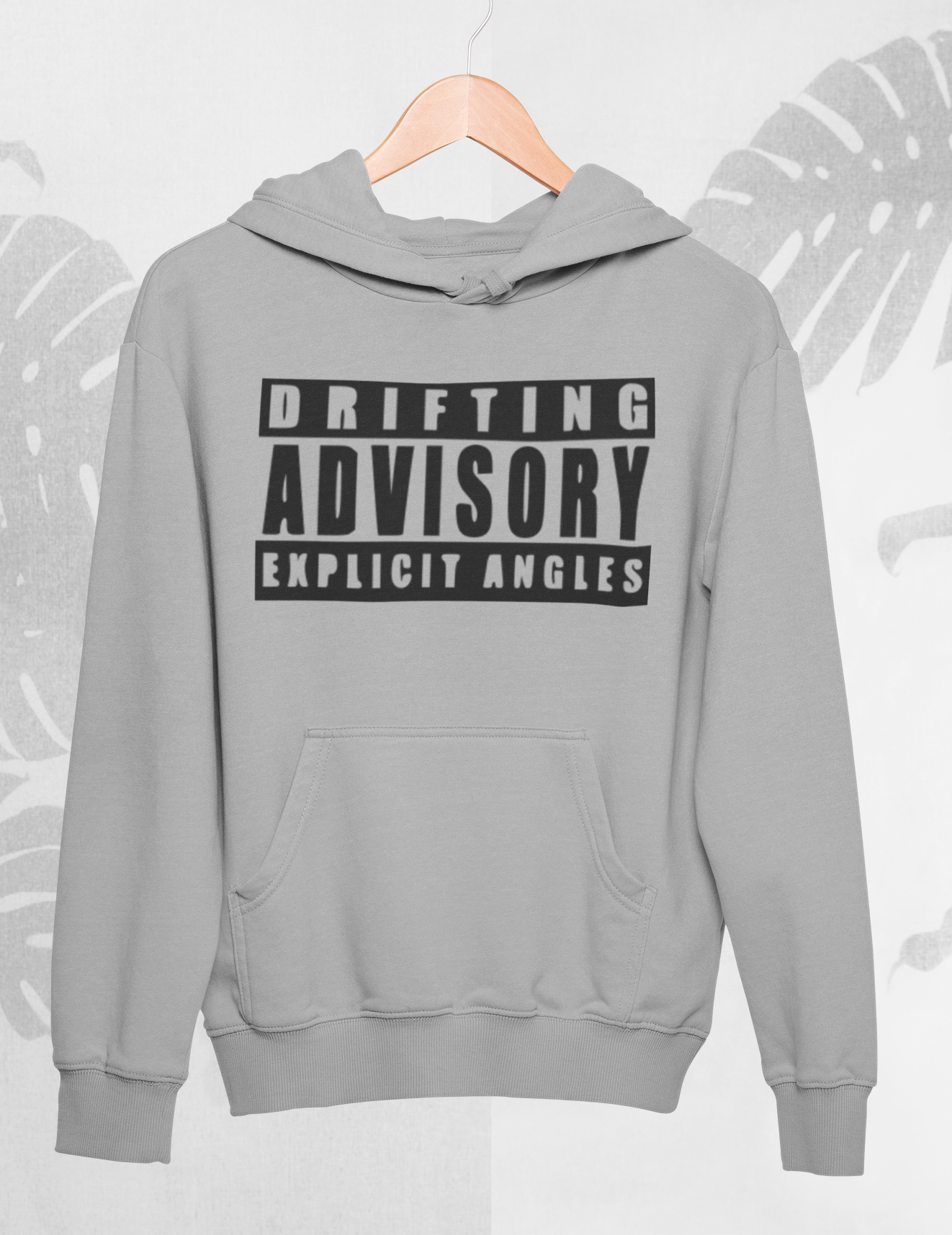 Gray hoodie with 'Drifting Advisory Explicit Angles' text on a light gray background with leaf patterns.