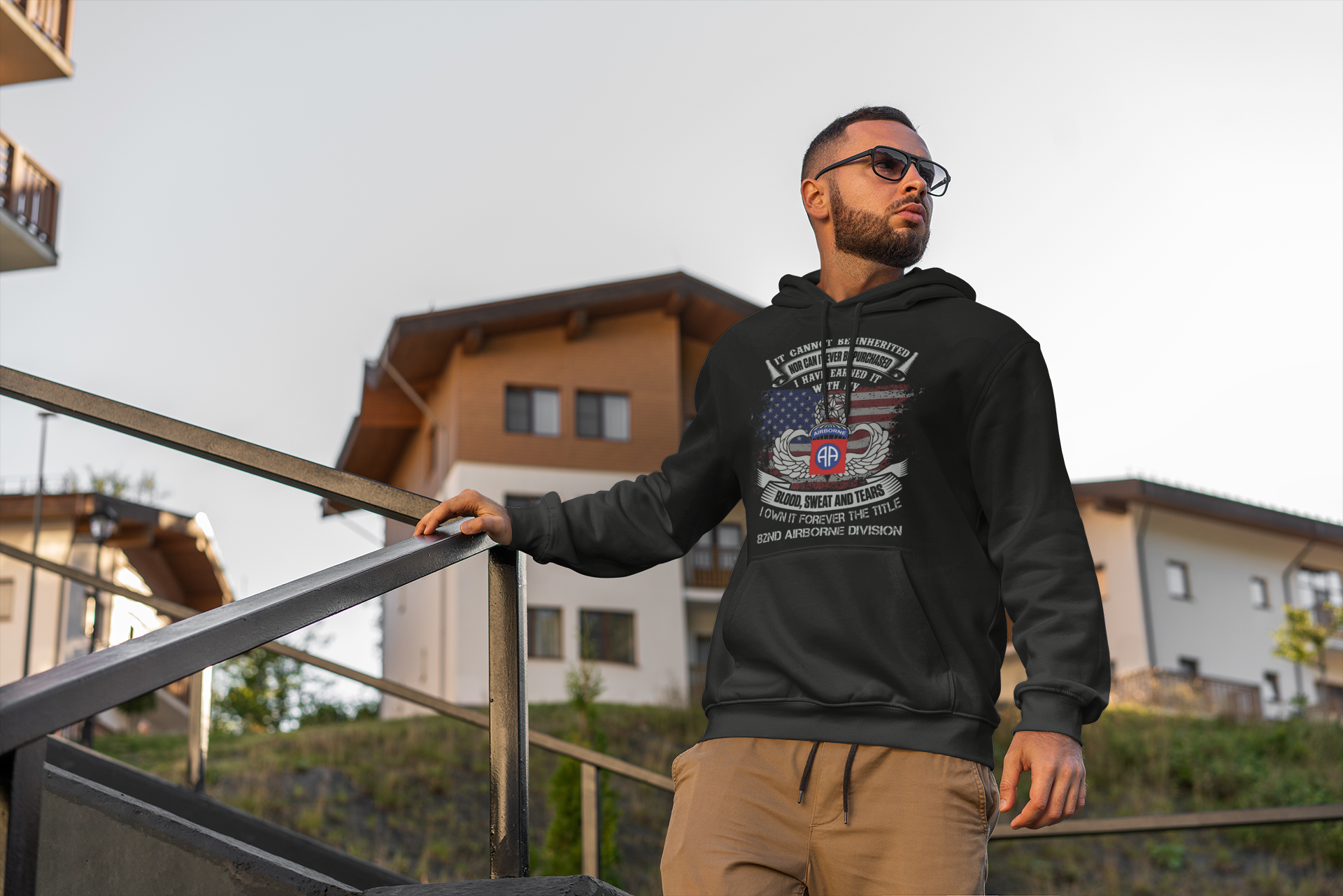 Man wearing a black hoodie with a graphic design, standing outdoors near a building.