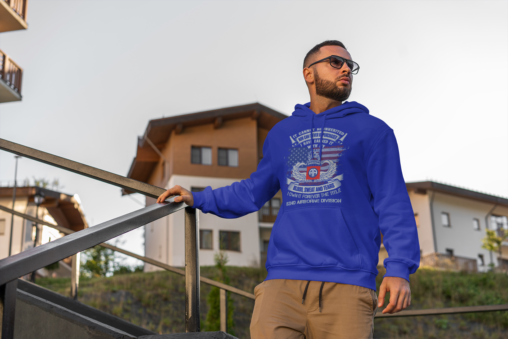 Man wearing a blue hoodie with a graphic design, standing outdoors near a building.
