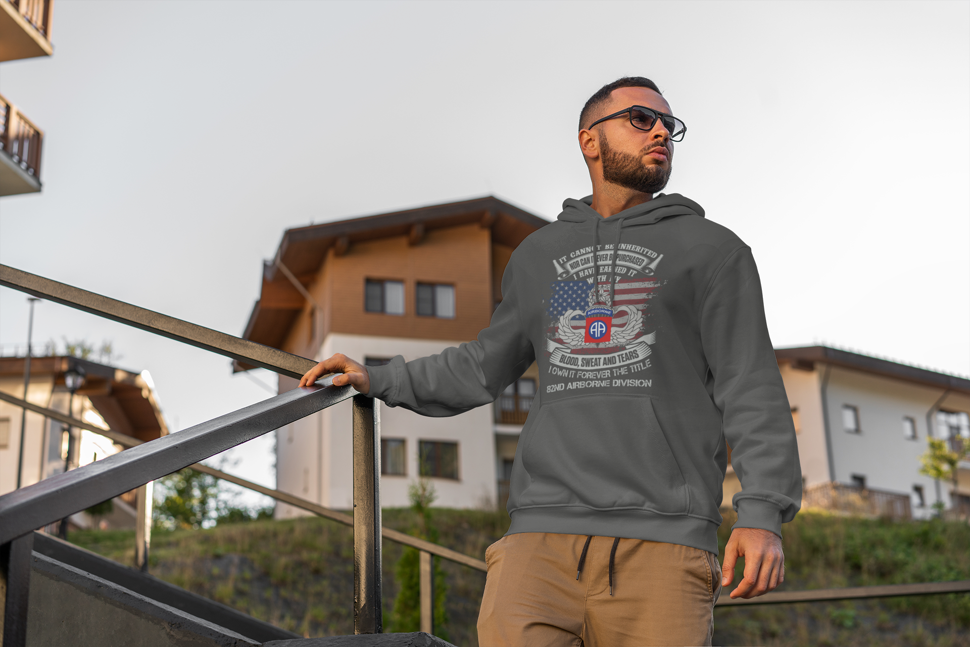 Man wearing a gray hoodie with a graphic design, standing outdoors near a building.