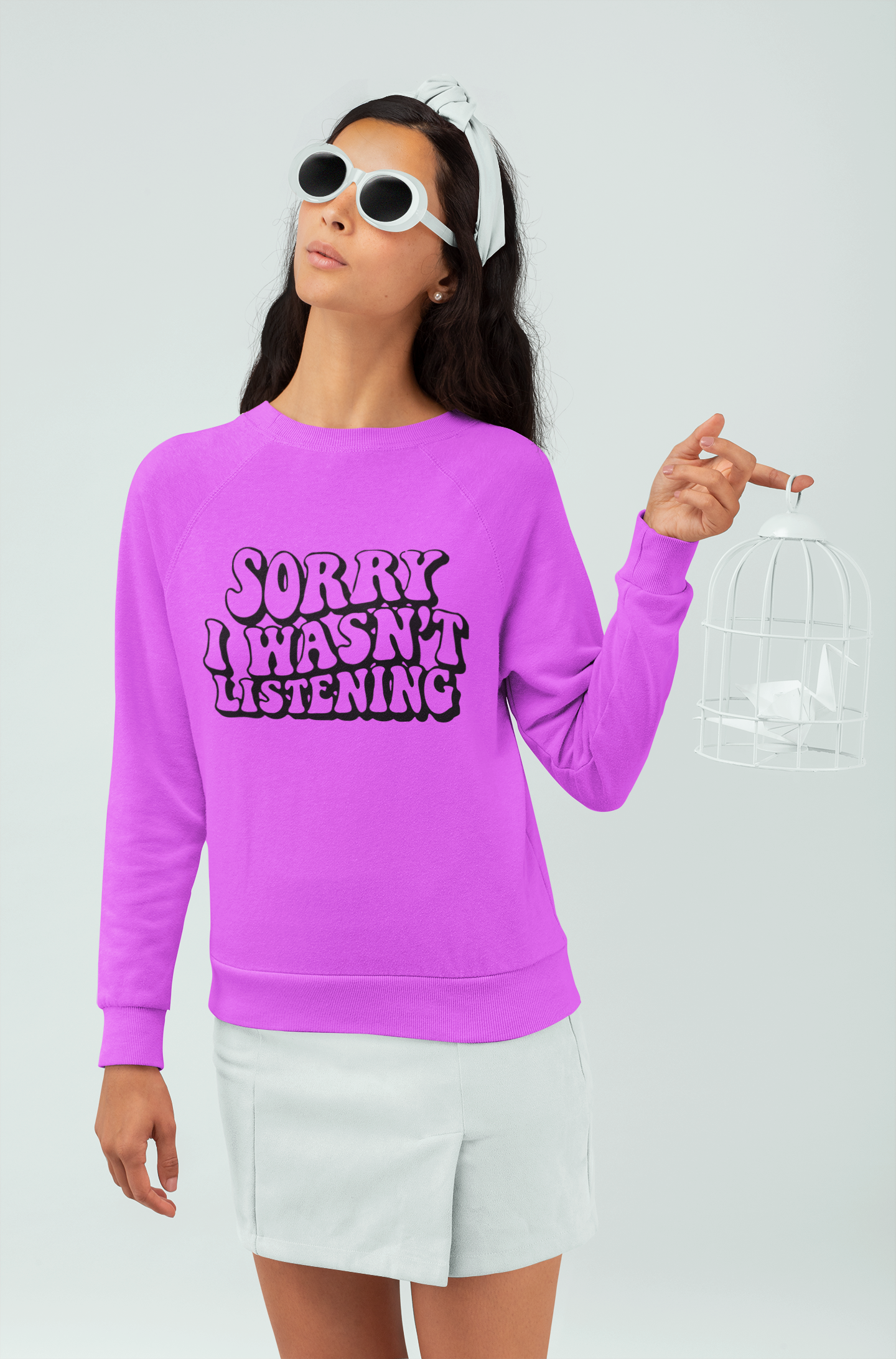 Person wearing a pink sweatshirt with text, white shorts, and sunglasses on a light gray background