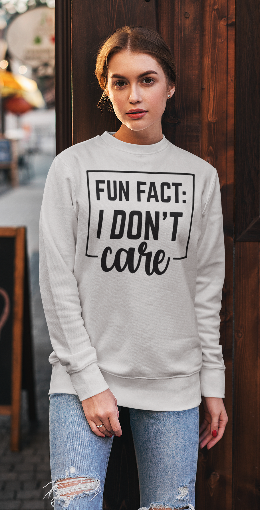 Woman wearing a gray sweatshirt with 'Fun Fact: I Don't Care' text on a street.