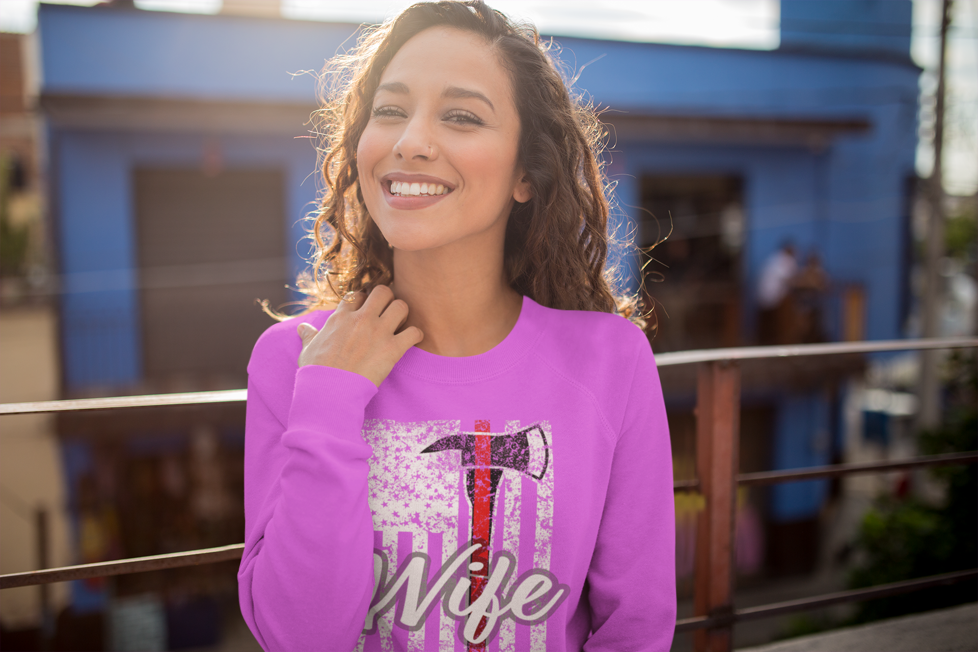 Woman wearing a pink sweatshirt with a graphic design and text, standing in front of a blue building.