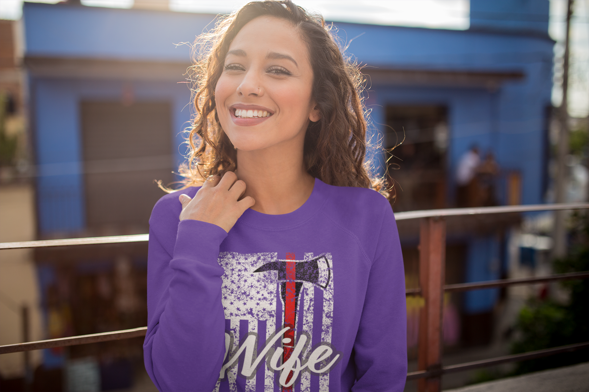 Woman wearing a purple sweatshirt with a graphic design in front of a blue building.