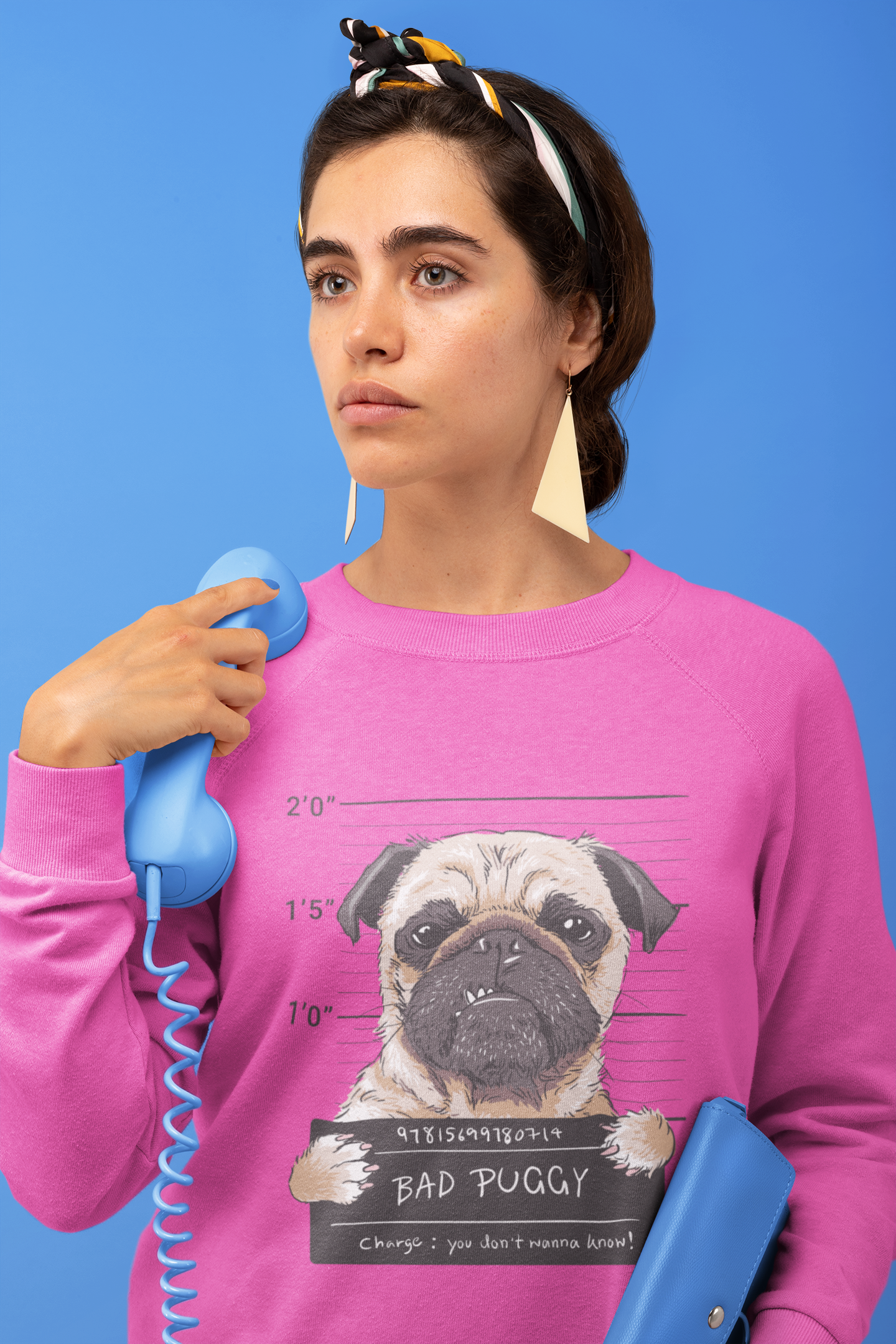 Woman wearing a pink sweater with a pug design, holding a blue phone against a blue background