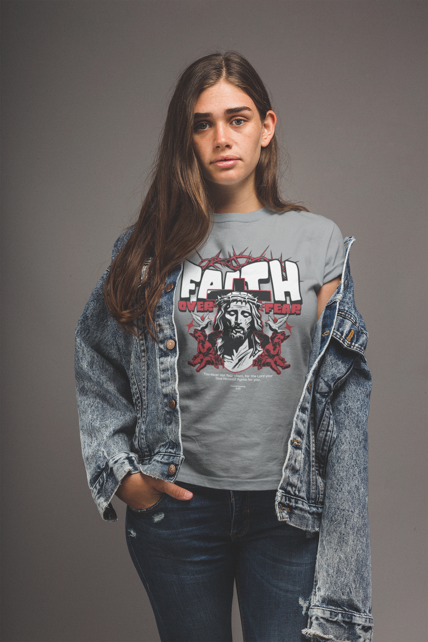 Person wearing a gray t-shirt with graphic design and denim jacket on a gray background