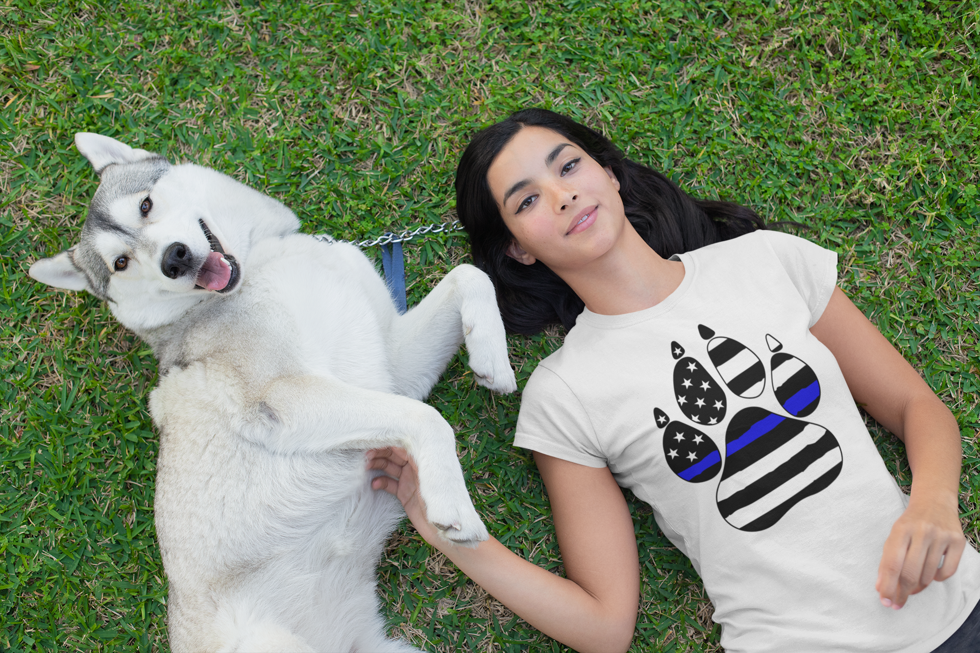 Woman lying on grass with a white dog, wearing a t-shirt with a paw print design.