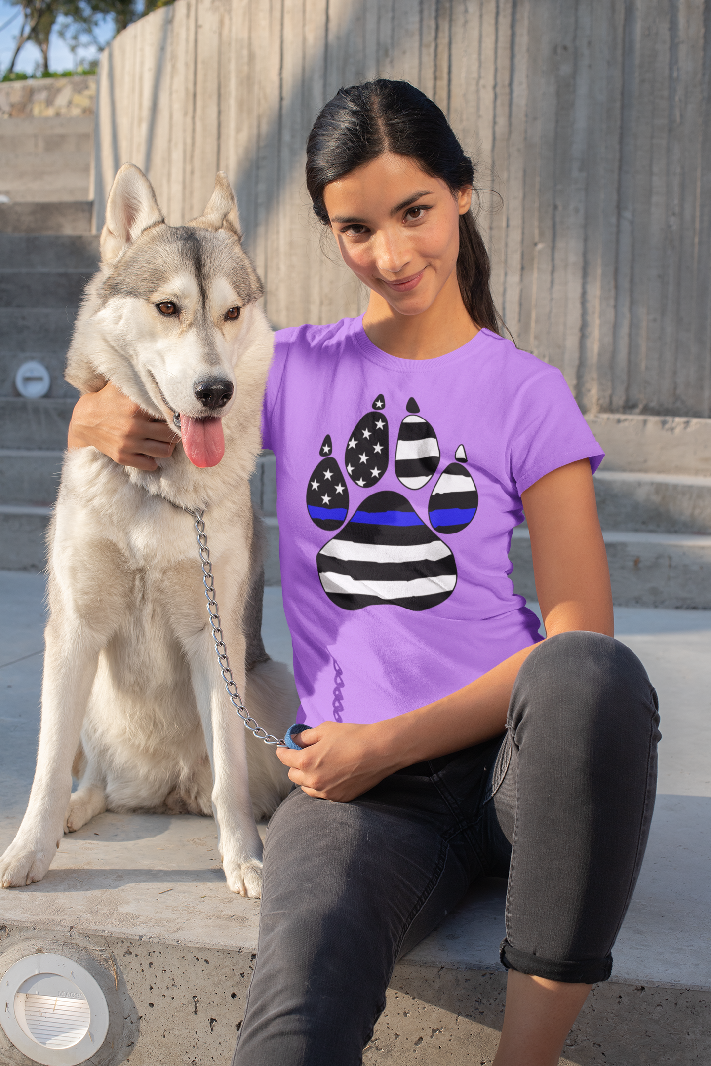 Woman sitting with a dog wearing a purple t-shirt with a paw design.