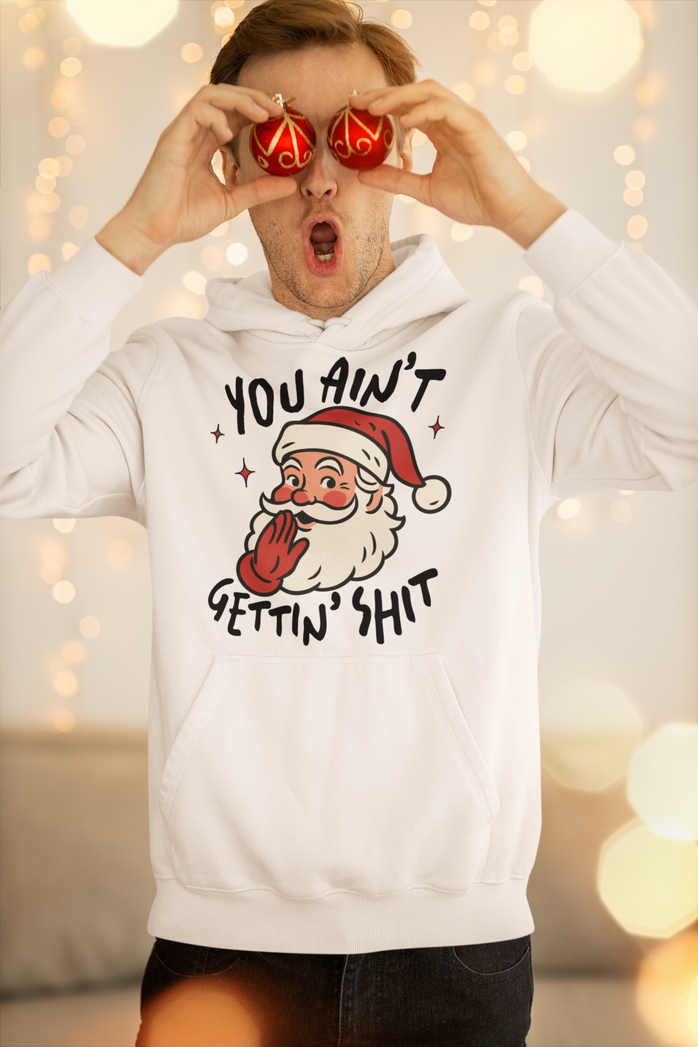 Person wearing a white hoodie with a graphic design of Santa Claus and text, against a blurred indoor background with lights.
