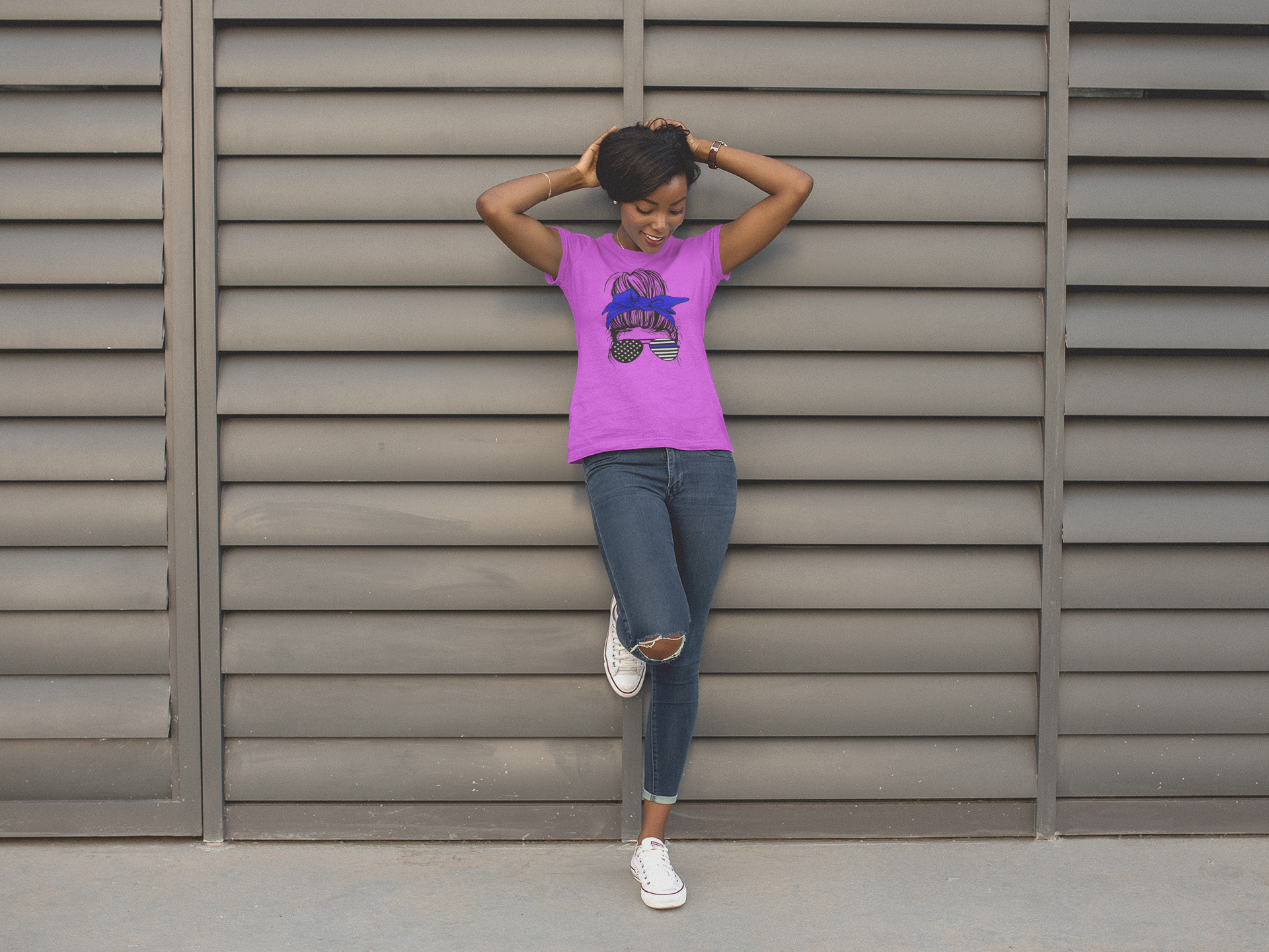 Woman in a pink shirt and jeans leaning against a metallic wall.